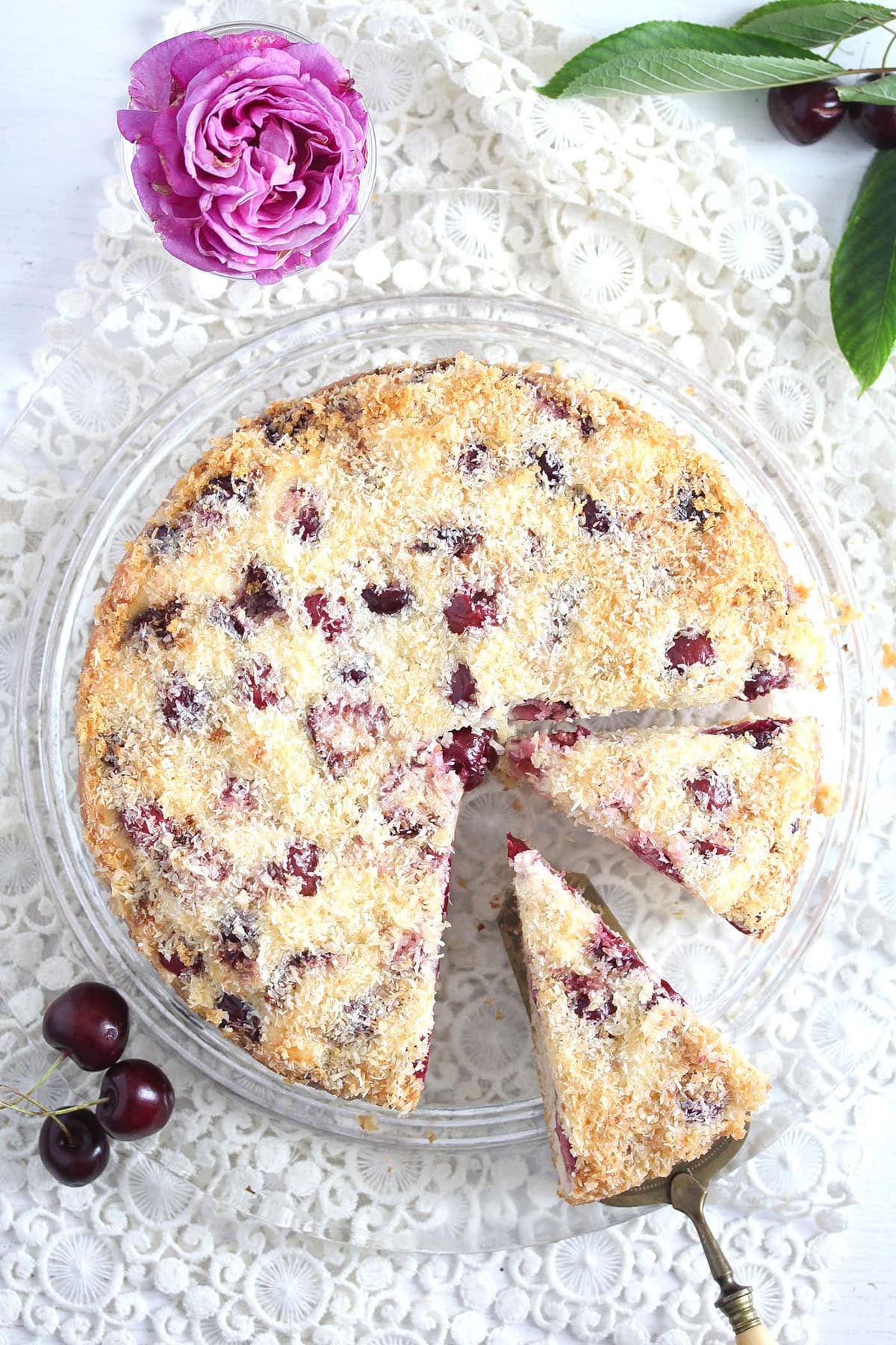 beautiful coconut and cherry cake sliced on a platter and a flour near it.