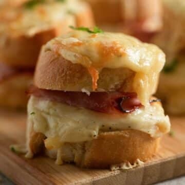 mini croque monsieur oozing with melted cheese on a wooden board.