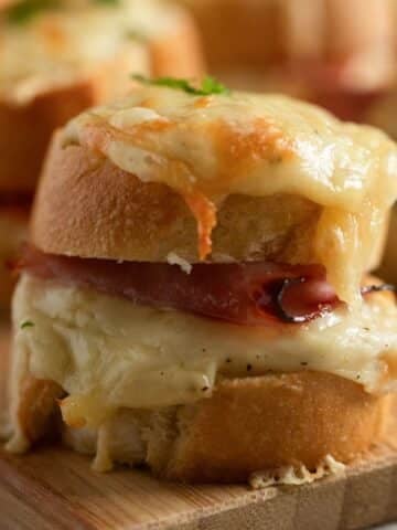 mini croque monsieur oozing with melted cheese on a wooden board.