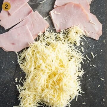 thin ham slices and grated cheese on a cutting board.