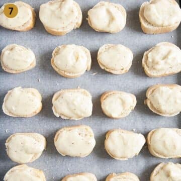 small baguette slices topped with bechamel on a lined baking sheet.
