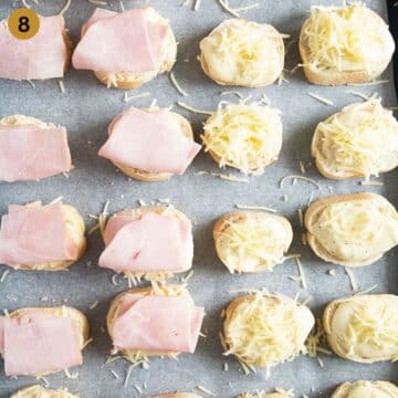 topping croque monsieur baguette slices with sauce, ham and cheese.