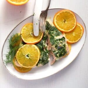 a piece of orange dill salmon served with oranges slices.
