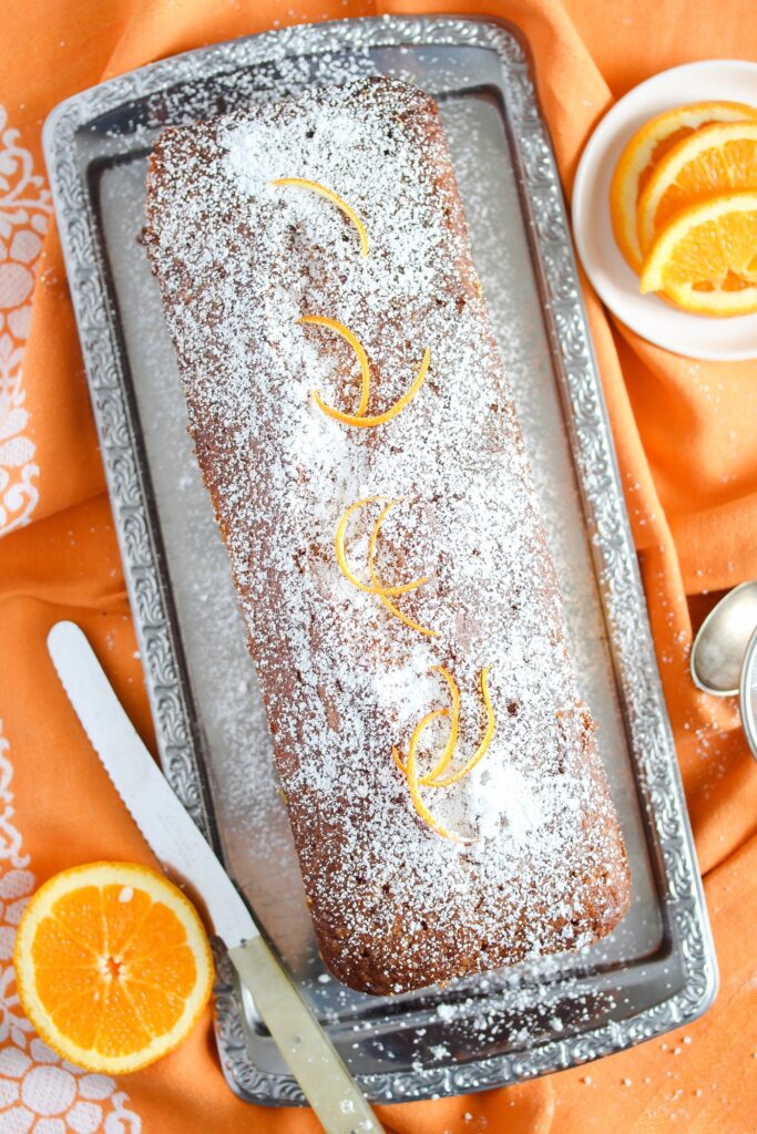 loaf cake on an orange table cloth sprinkled with icing sugar