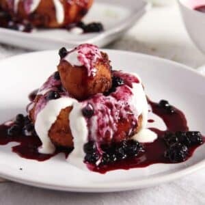 romanian dessert papanasi served with smetana and runny jam on a small plate.