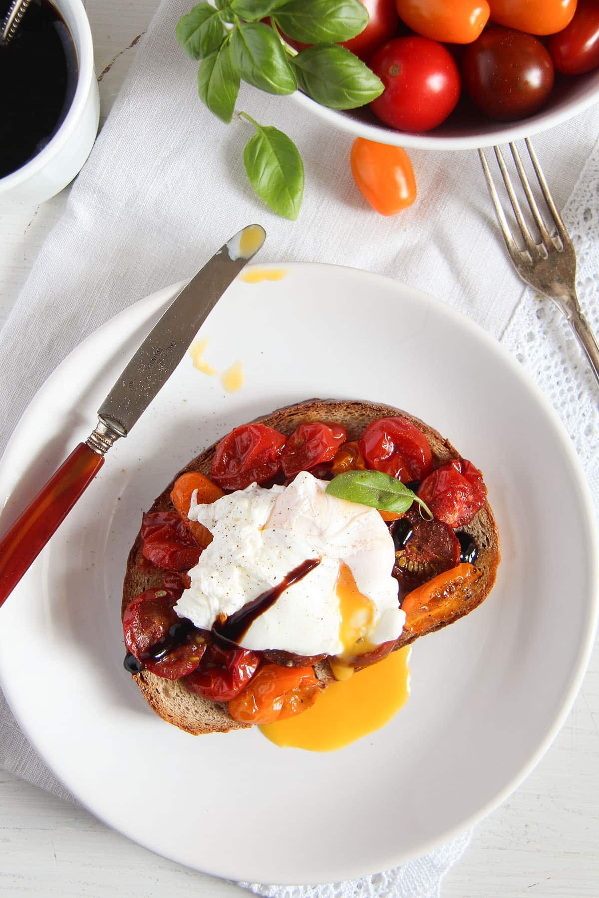 roasted cherry tomatoes and poached egg on toast on a plate with a knife.