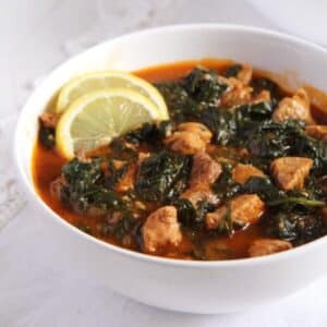 bowl of pork and chicken stew garnished with two lemon slices.