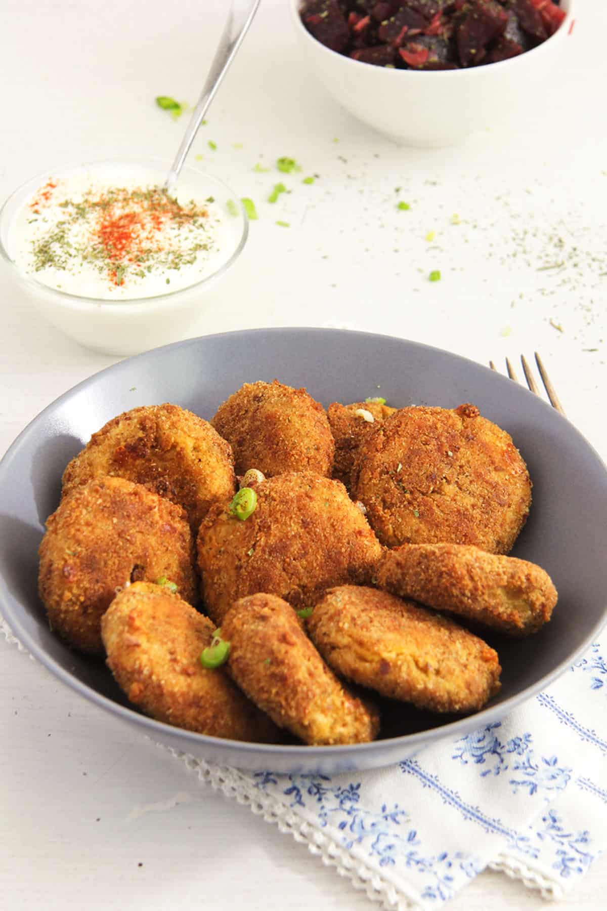 Cauliflower Potato Patties Dish nine crispy cauliflower potato cakes in a bowl, smalls bowls with yogurt dip and beet salad behind.
