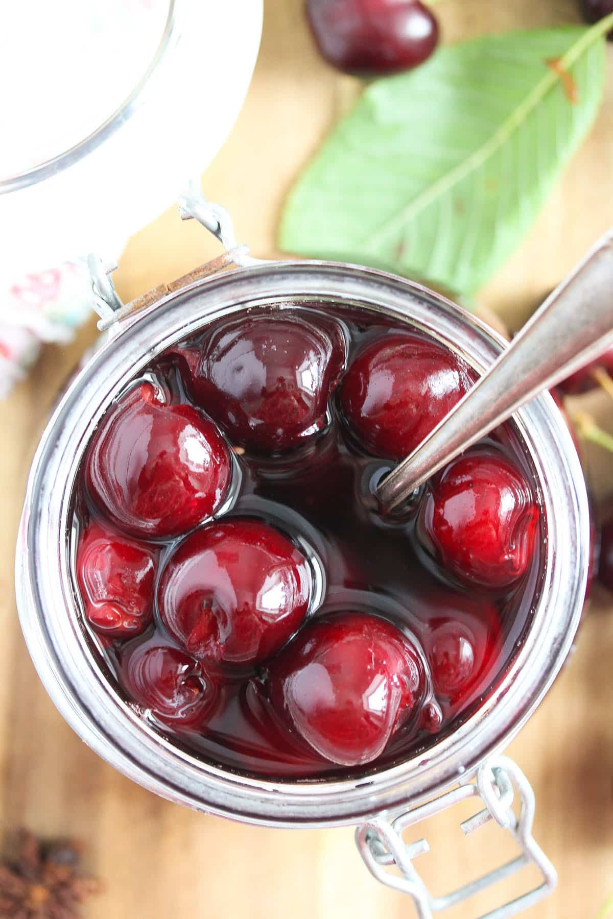 a jar of red wine cherries and a cherry leaf on a wooden board.