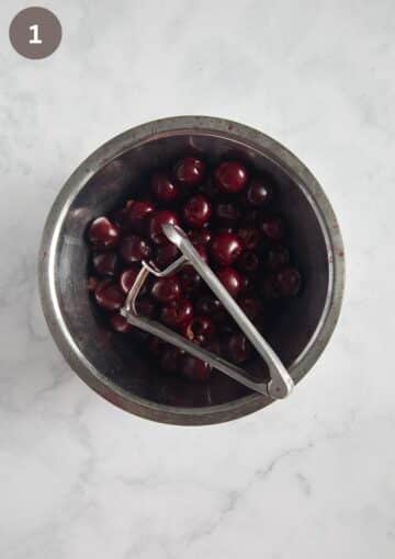 pitted cherries in a bowl and a cherry pitter on top.