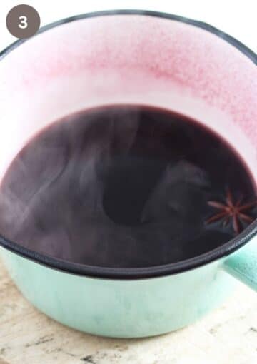 cooking red wine with spices in a small green saucepan.
