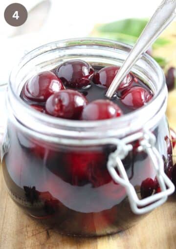 cherries covered with red wine in a jar with a spoon in it.