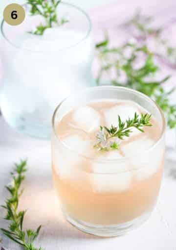 a glass with rhubarb gin and another one full of ice cubes behind it.