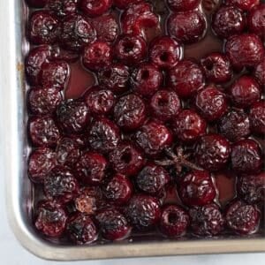 shrivelled roasted cherries and a star anise in a roasting pan.