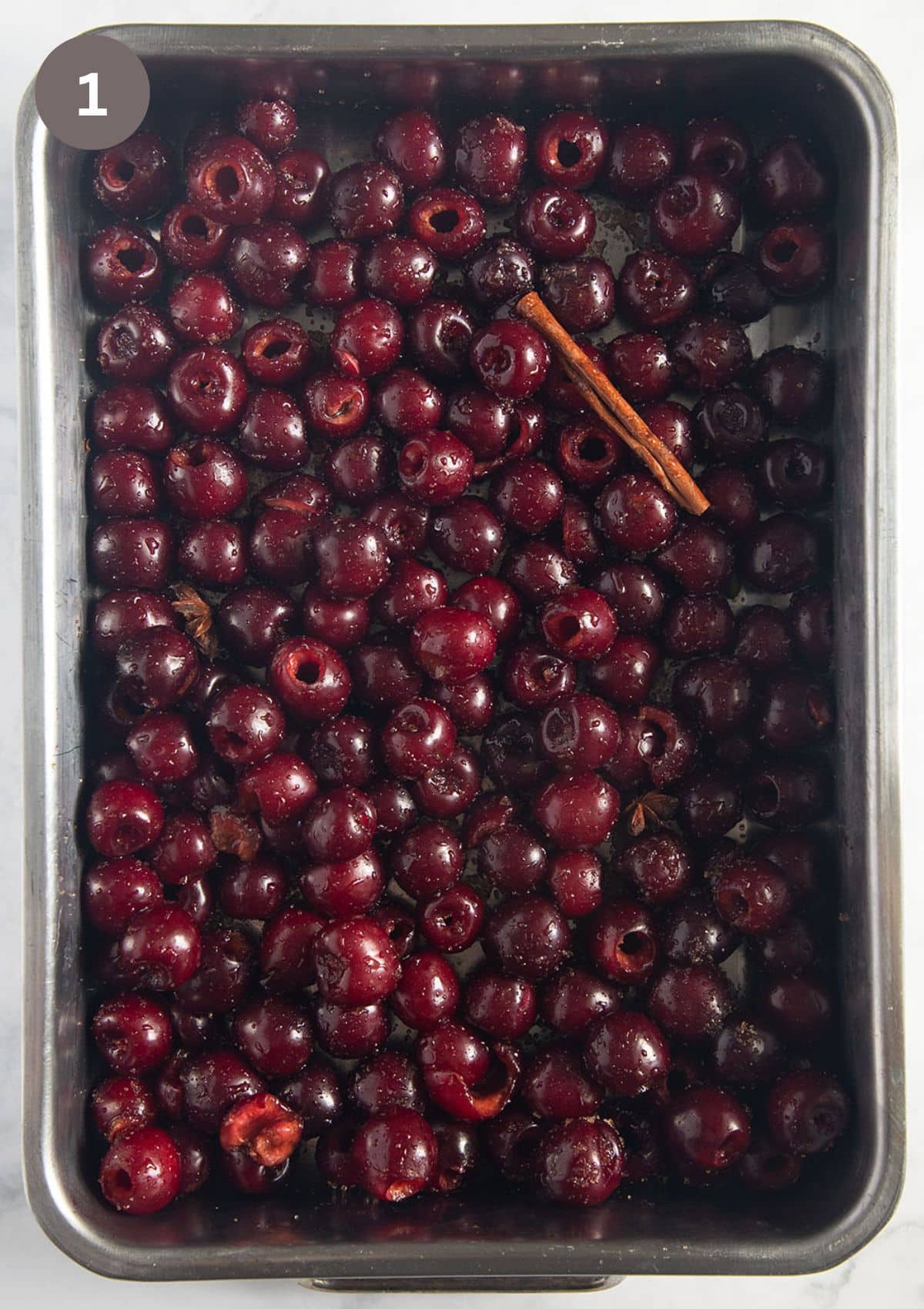 a roasting tin full of cherries, a cinnamon stick, and a star anise in before roasting.