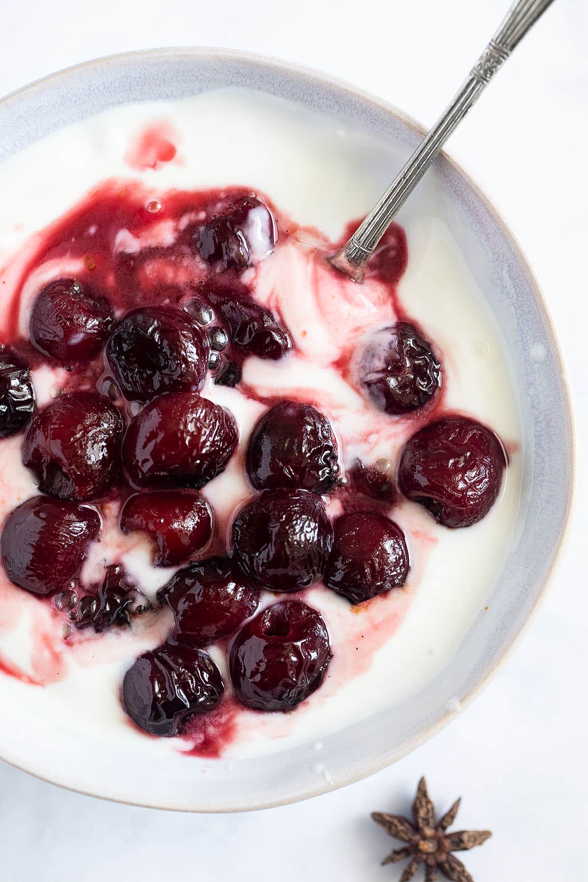roasted cherries served with yogurt in a small bowl with a spoon in it.