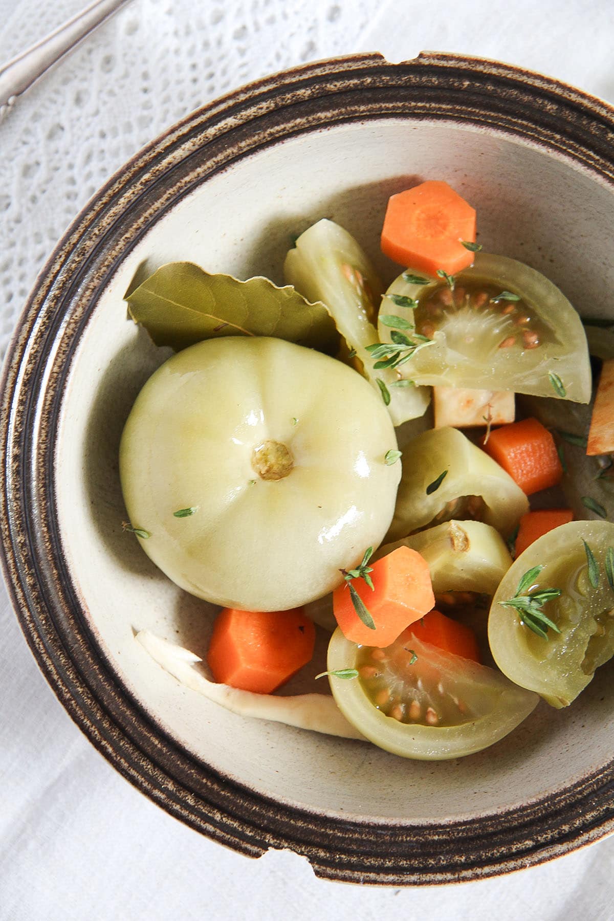 one whole pickled green tomato and another sliced one with carrots in a chipped bowl.