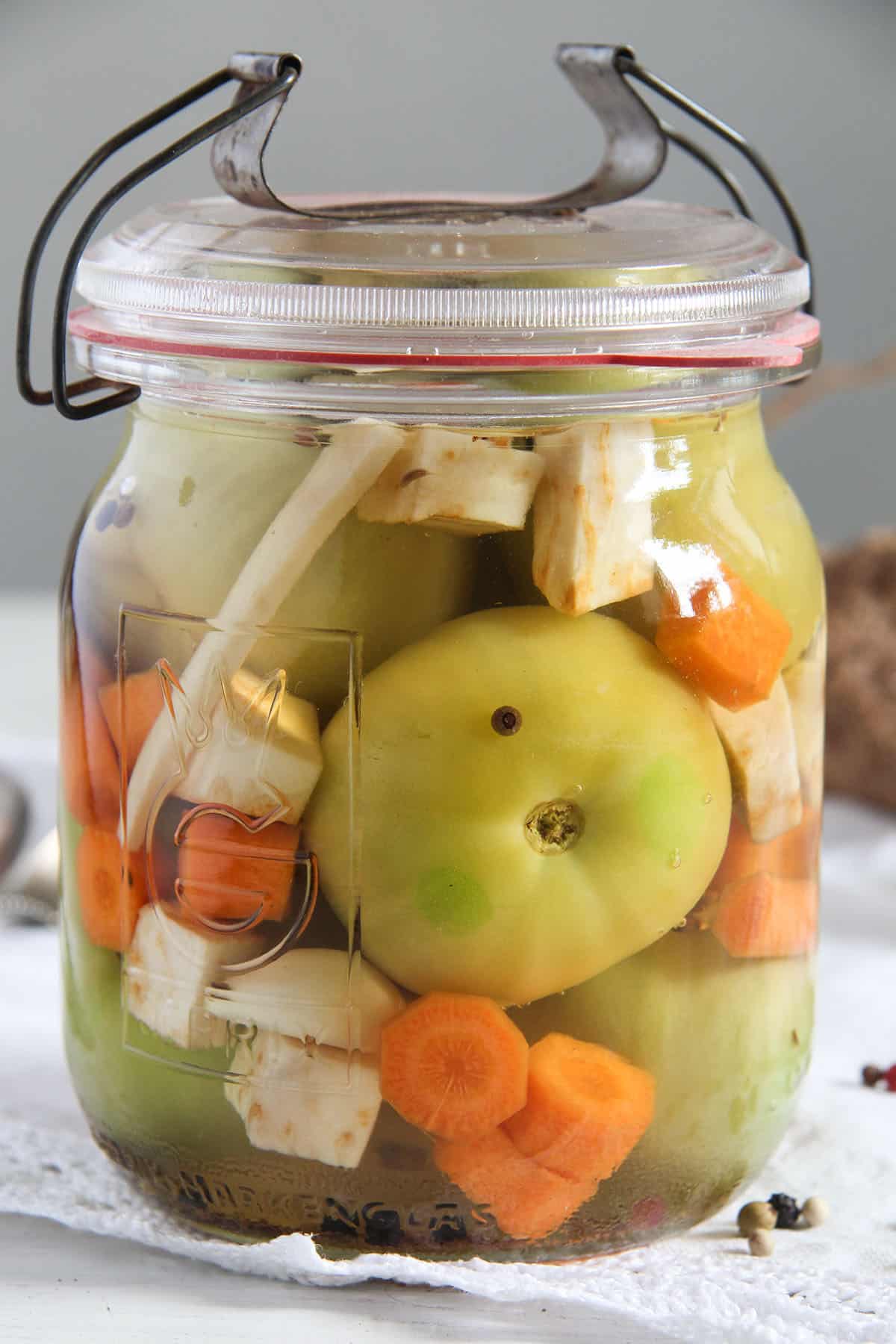 romanian green tomato pickles with horseradish and carrots in a jar.