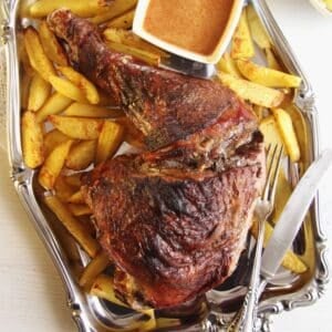 large slow roasted turkey leg served with roasted potatoes and a bowl of gravy on a silver platter.