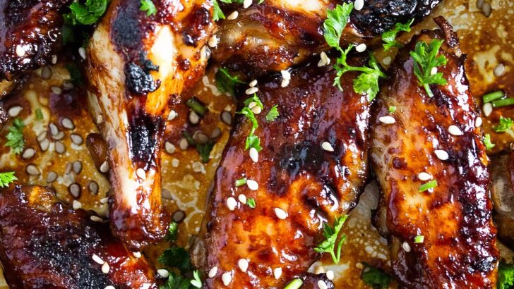 many dark brown sticky wings sprinkled with sesame seeds and parsley.