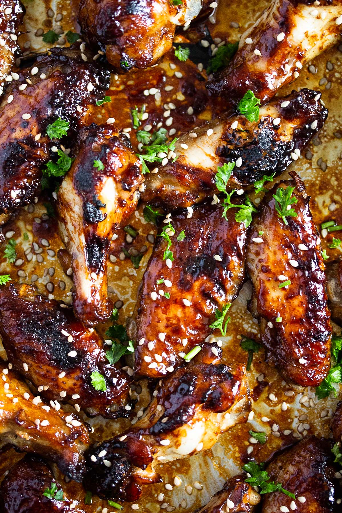 many dark brown sticky wings sprinkled with sesame seeds and parsley.