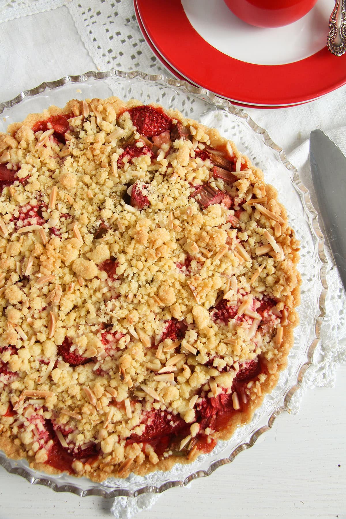 strawberry and rhubarb tart with crumbles on top on a glass platter.