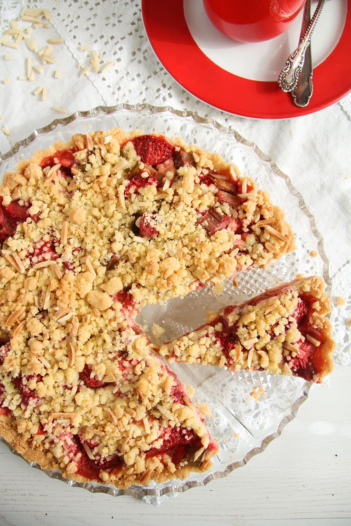 overhead view of a strawberry crumble tart with rhubarb on a serving platter. 