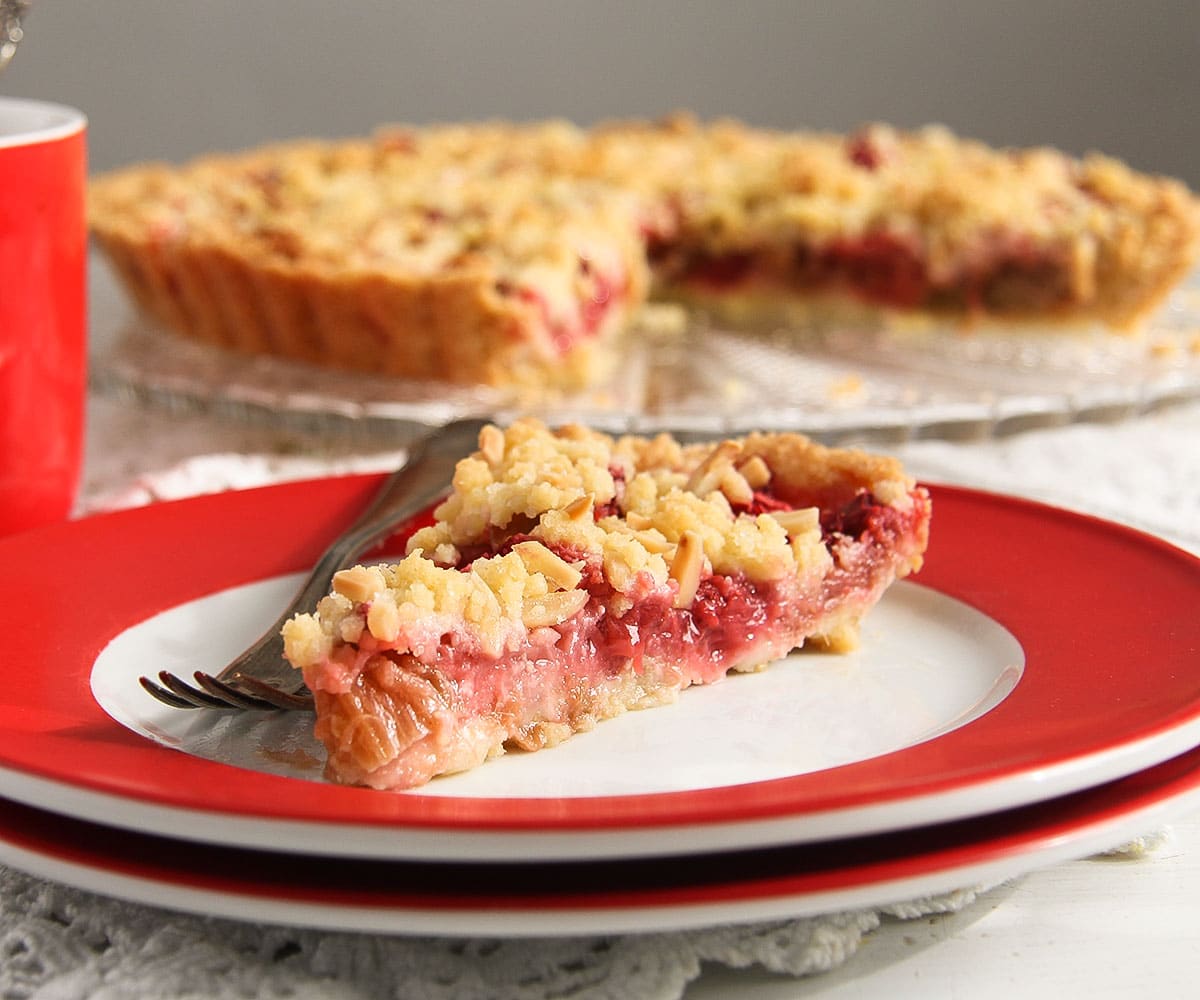 one slice of rhubarb crumble tart with strawberries on a white plate with red margins.