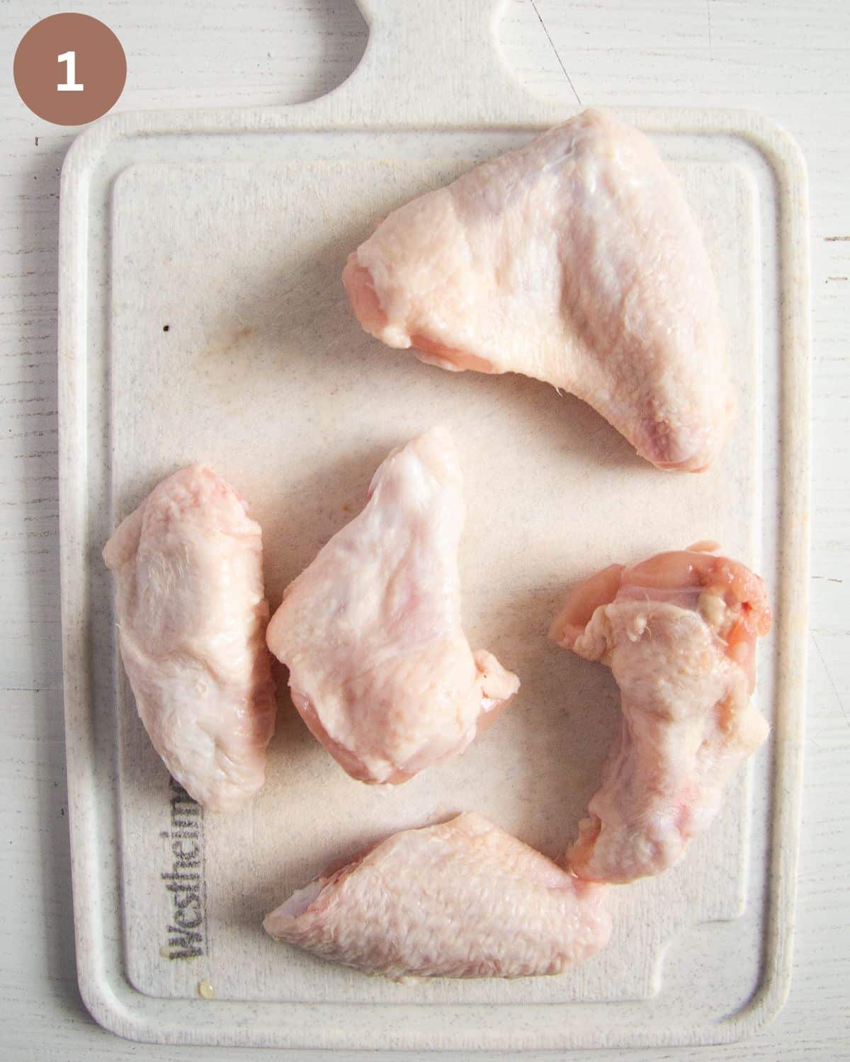 raw chicken wings on a small cutting board.