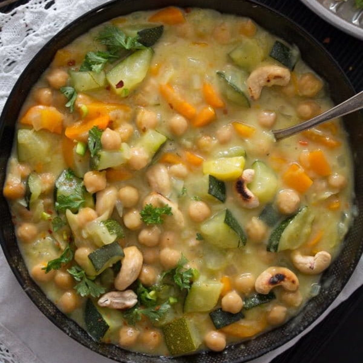 a bowl with creamy zucchini curry topped with roasted cashew nuts.