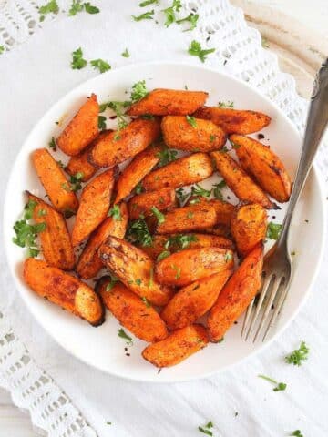 air fryer carrots sprinkled with parsley on a white plate with a fork
