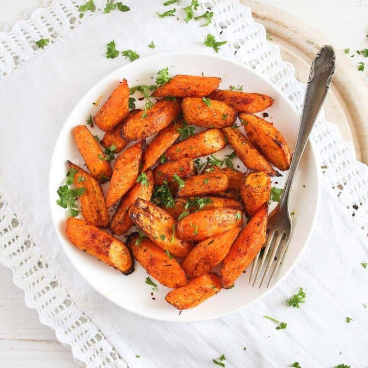 air fryer carrots sprinkled with parsley on a white plate with a fork