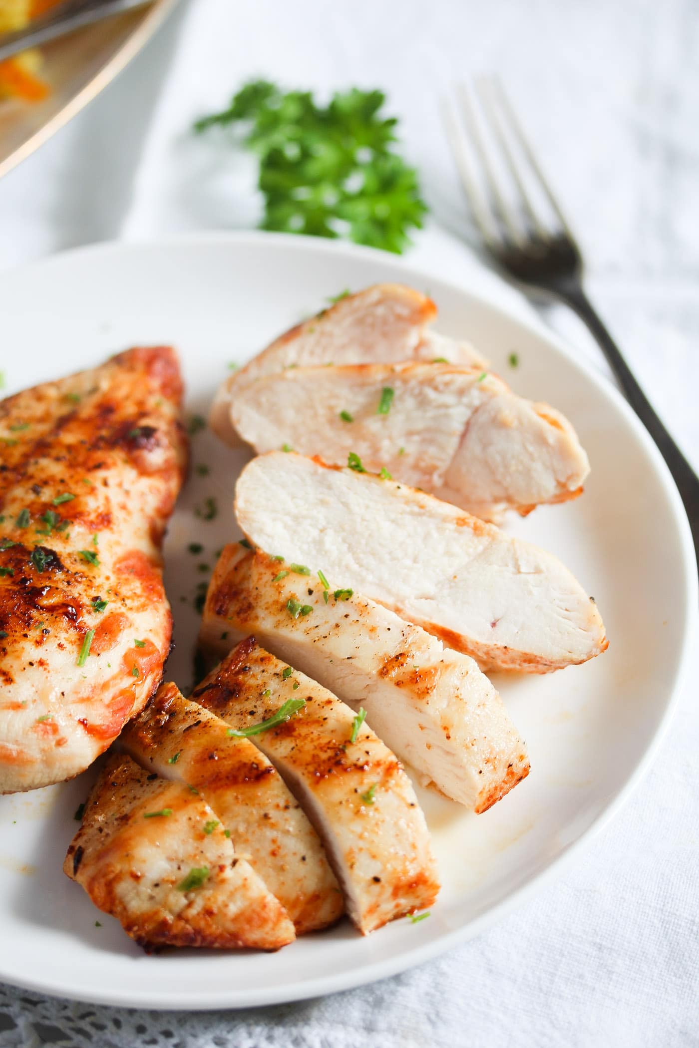 chicken breast slices on a white plate with parsley and a fork