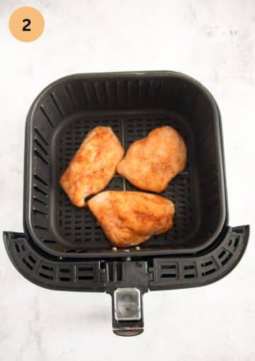 seasoned and frozen chicken breast pieces in an air fryer basket.