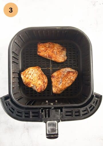 three pieces of golden chicken in the basket of an air fryer.