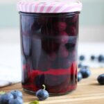 jar of preserved blueberries on a wooden board with fresh berries around