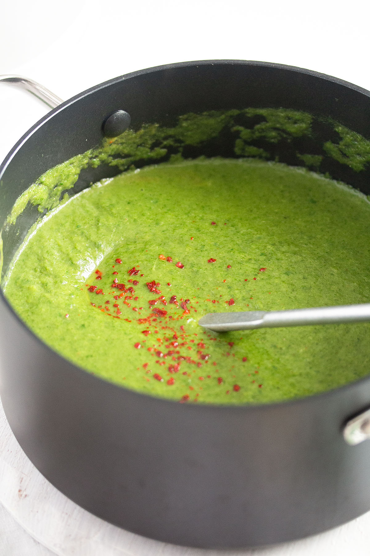full pot of green vegan broccoli soup sprinkled with chili flakes.