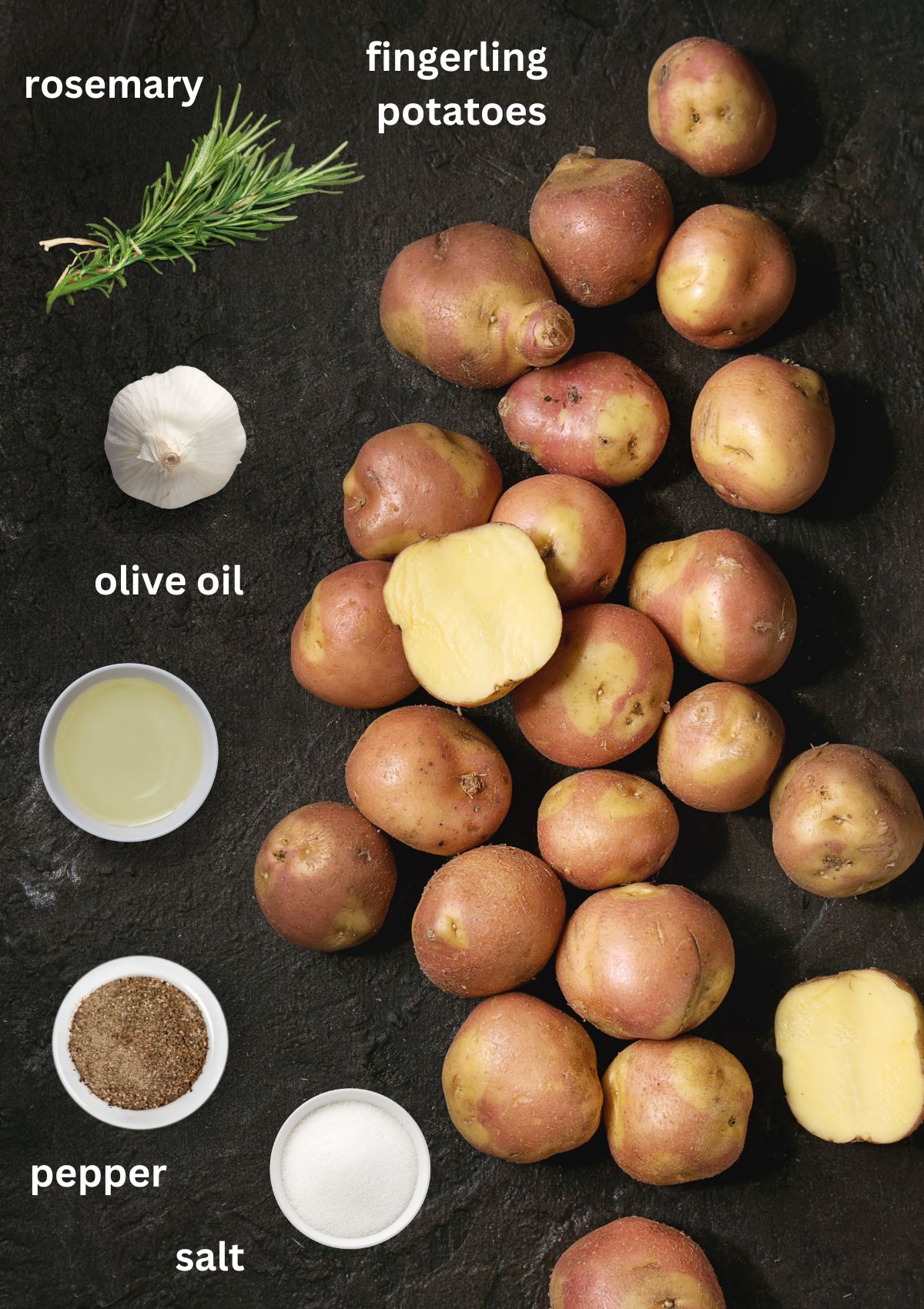 raw fingerling potatoes, salt, pepper, fresh rosemary and oil on a black table.