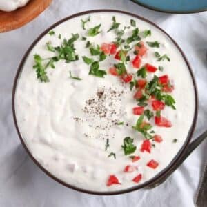 garlic sour cream sauce topped with finely chopped tomatoes and parsley in a bowl.