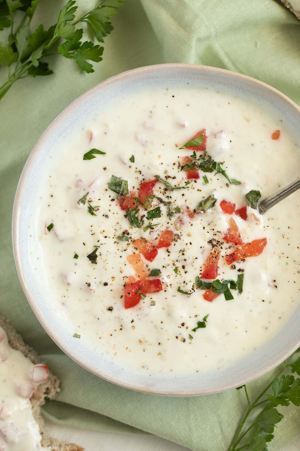 a bowl of sour cream garlic sauce, romanian-style, topped with chopped tomatoes and parsley.