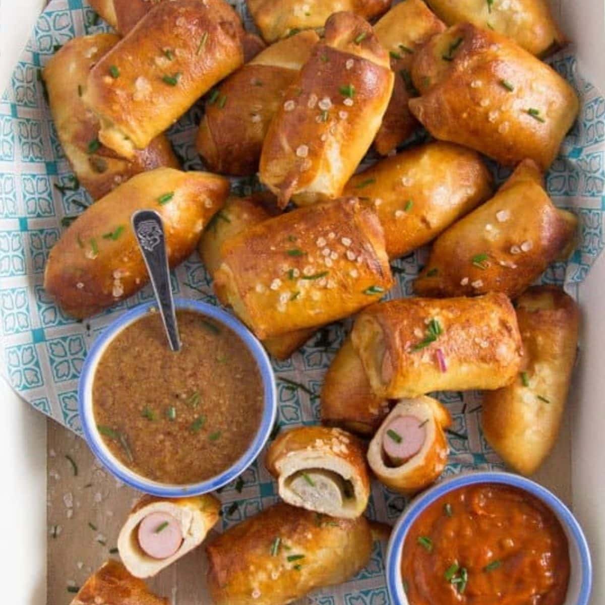 lots of small pretzel pigs in a blanket and two bowls with sweet mustard and curry ketchup.