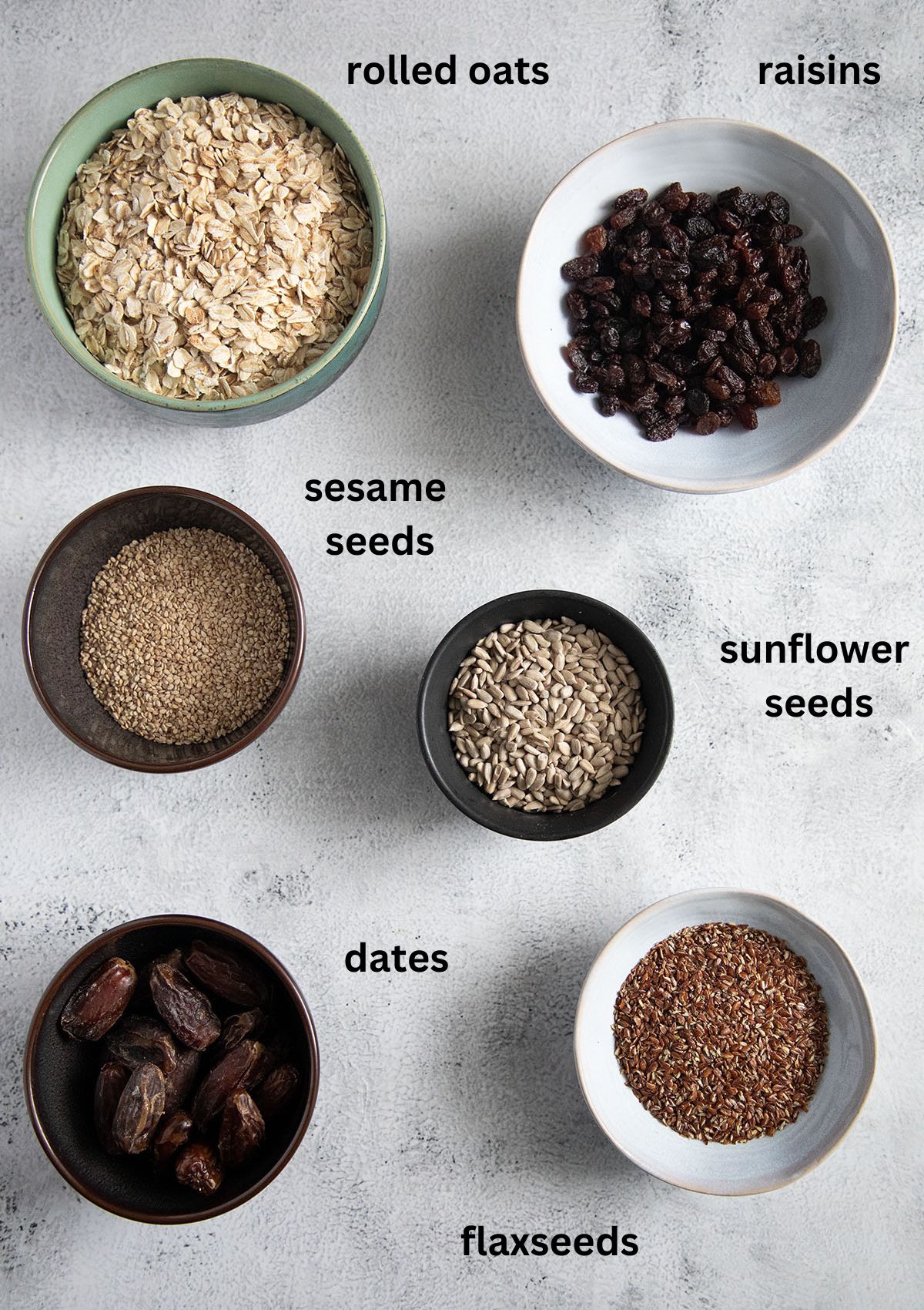 bowls with rolled oats, raisins, sesame seeds, sunflower seeds, flaxseeds, and dates for mixing muesli.