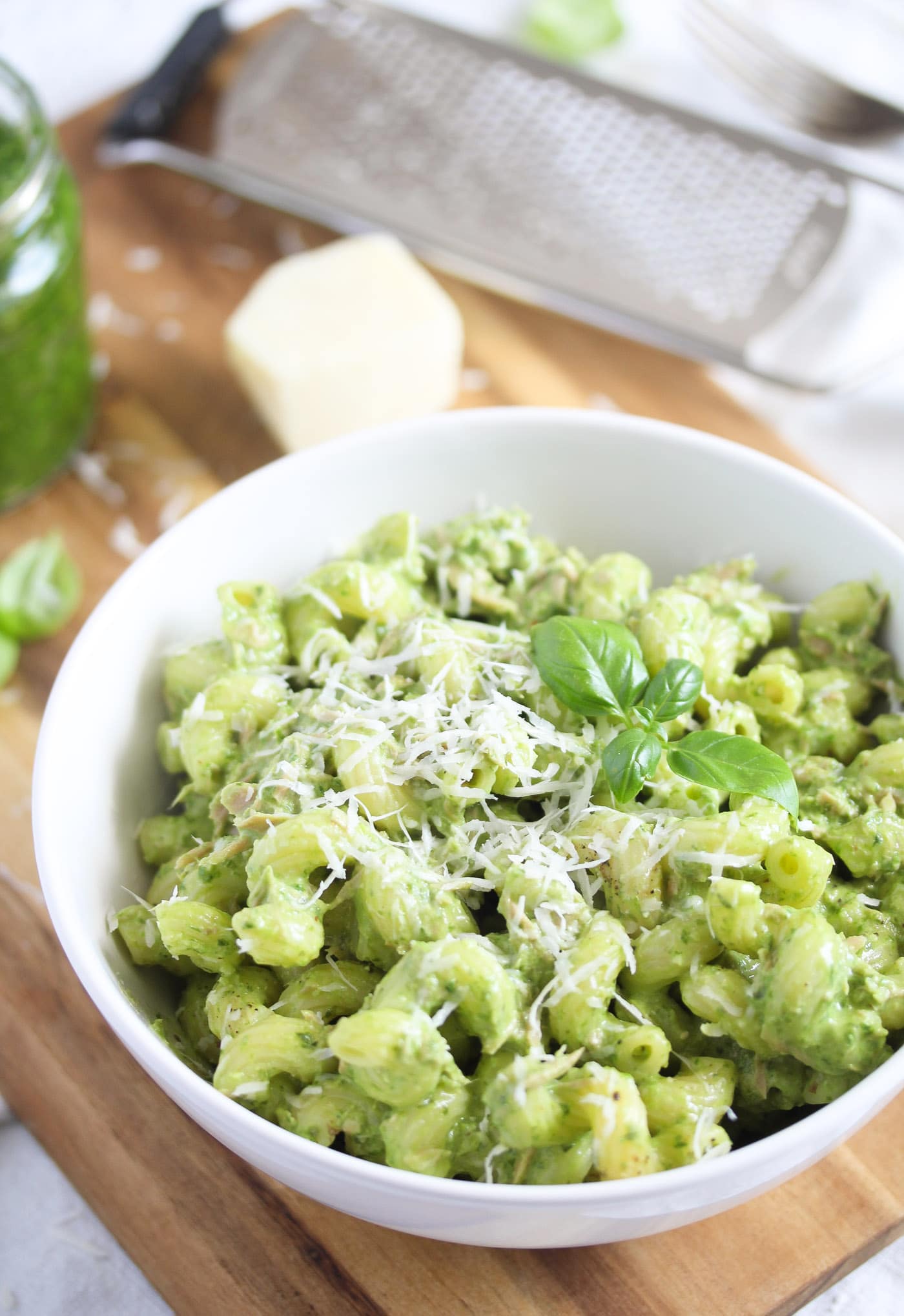 bowl of pesto pasta with tuna with parmesan grater and jar of pesto in the back