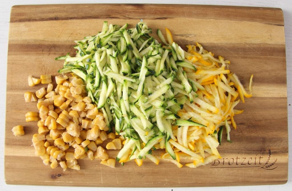 grated green and yellow zucchini and corn kernels on a wooden board