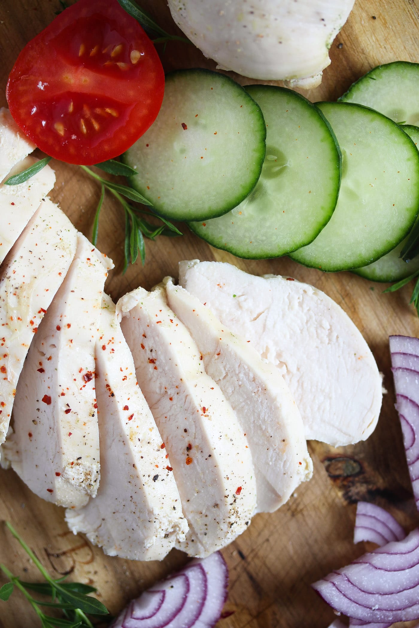 sliced boiled chicken breast on a wooden board with cucumbers.