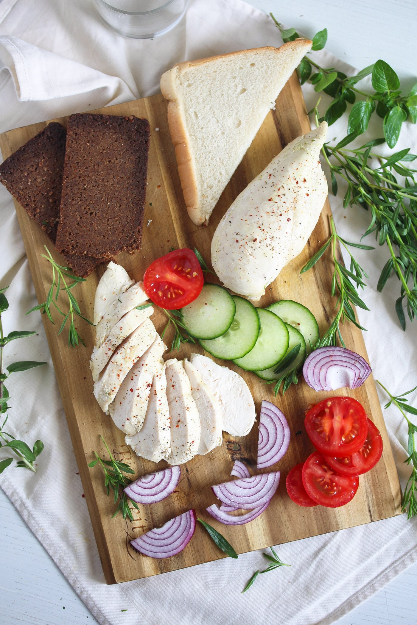wooden board with poached chicken breast, dark bread and vegetables