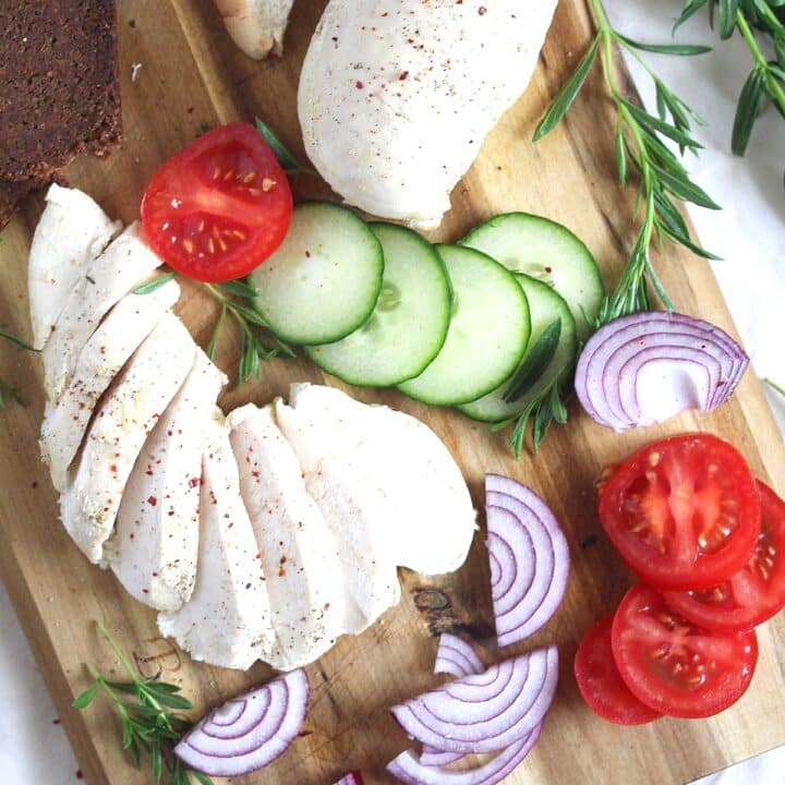 boiled frozen chicked breast sliced on a wooden board with tomatoes and red onions.