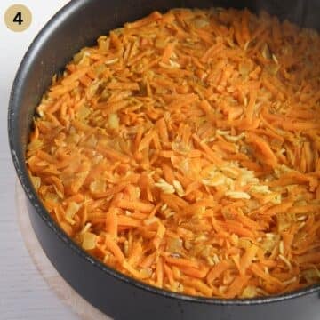 cooked grated carrots on top of cooked rice in a saucepan.