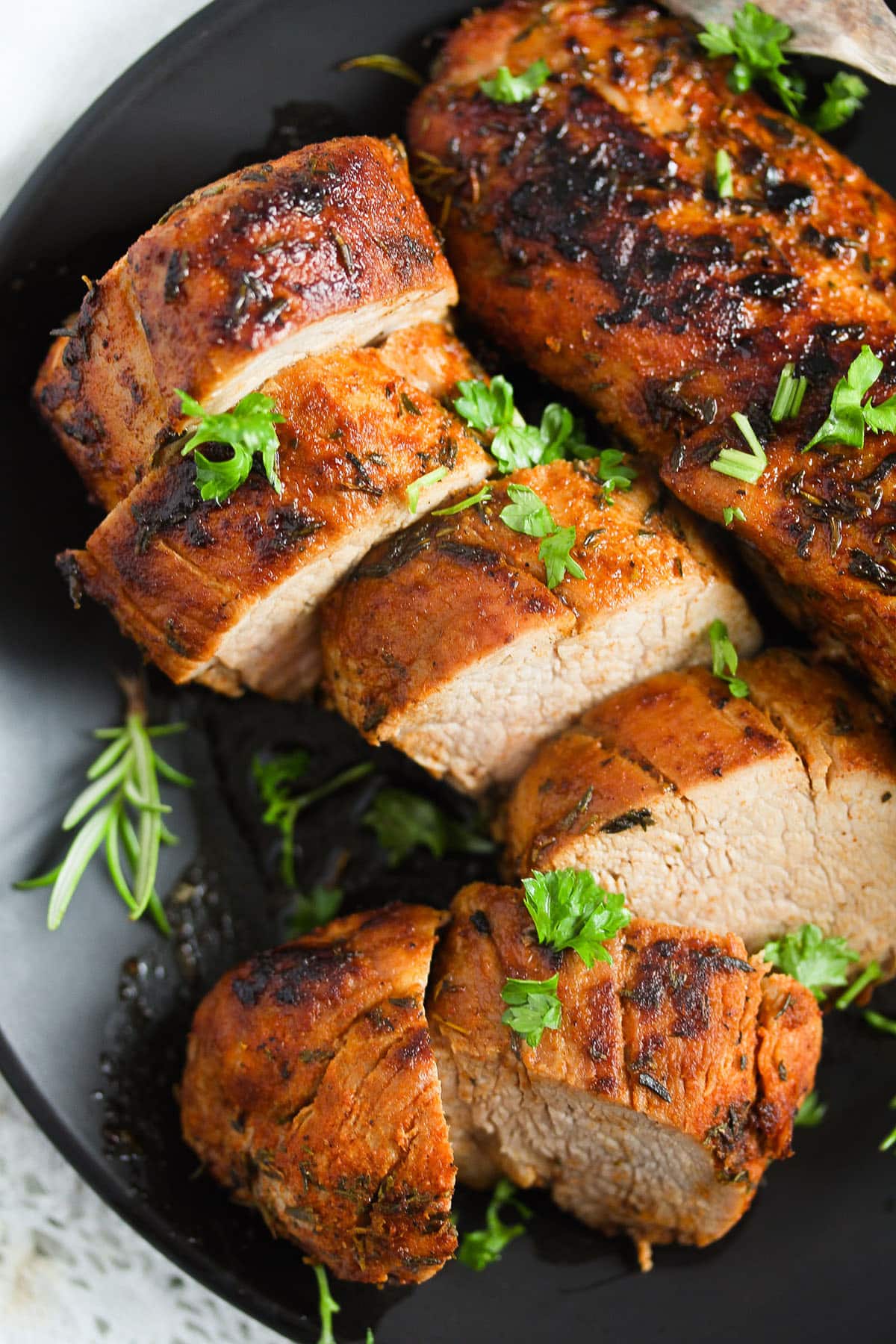 thickly sliced cast iron skillet pork tenderloin sprinkled with fresh parsley.