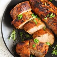 sliced cast iron pork tenderloin on a black plate.